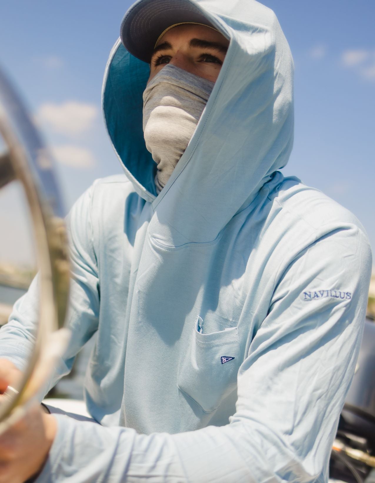 Model driving a boat wearing the Light Ocean Blue Angler Crossover Bamboo Hoodie.